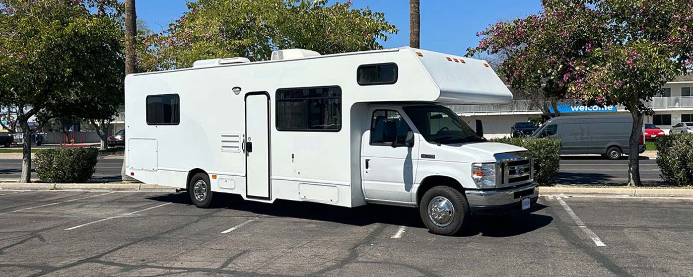 White RV with no Cruise America paint parked in parking lot.