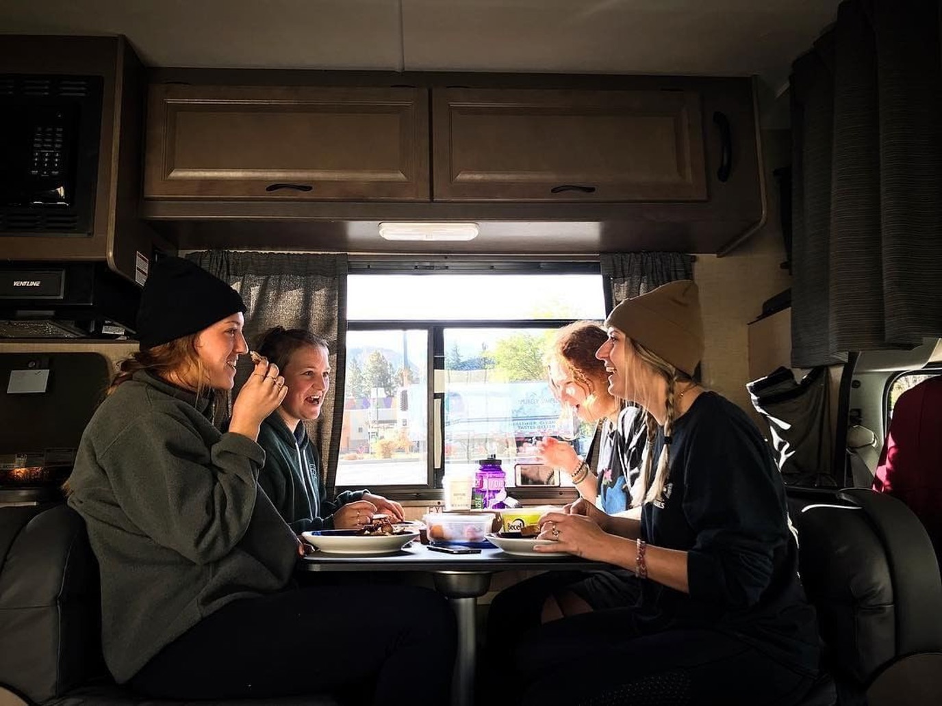 Four young women laughing and eating a meal at an RV table