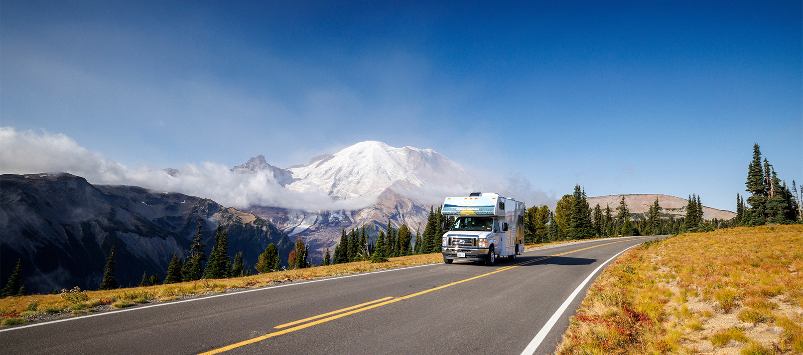 RV driving in front of a forest and mountain.