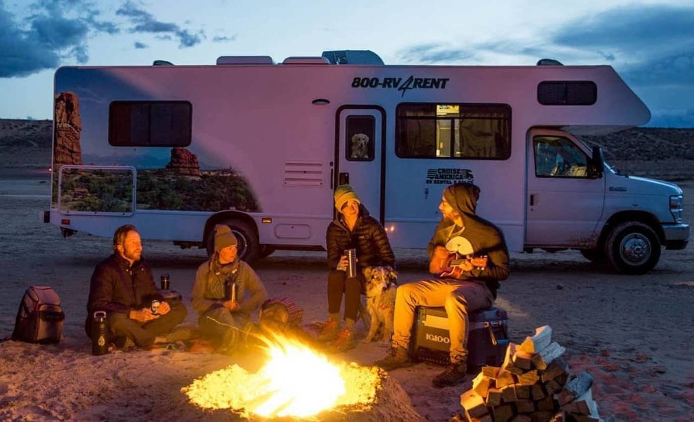 Group in front of campfire with Cruise America RV in background